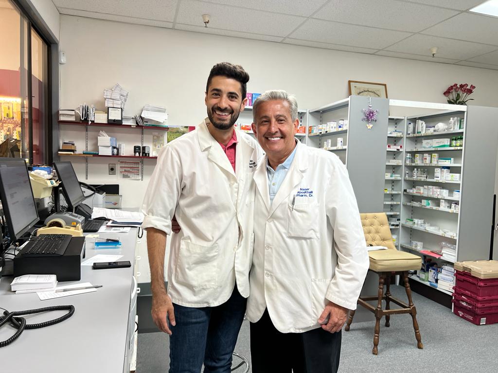 Akram AbouKhalil, PharmD, and his father Naser Kalil, PharmD, in white coats inside Oak Grove Pharmacy in Concord, California